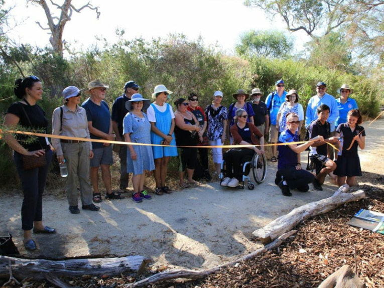 Group of people on a path in beautiful bush setting watching the cutting of a yellow ribbon